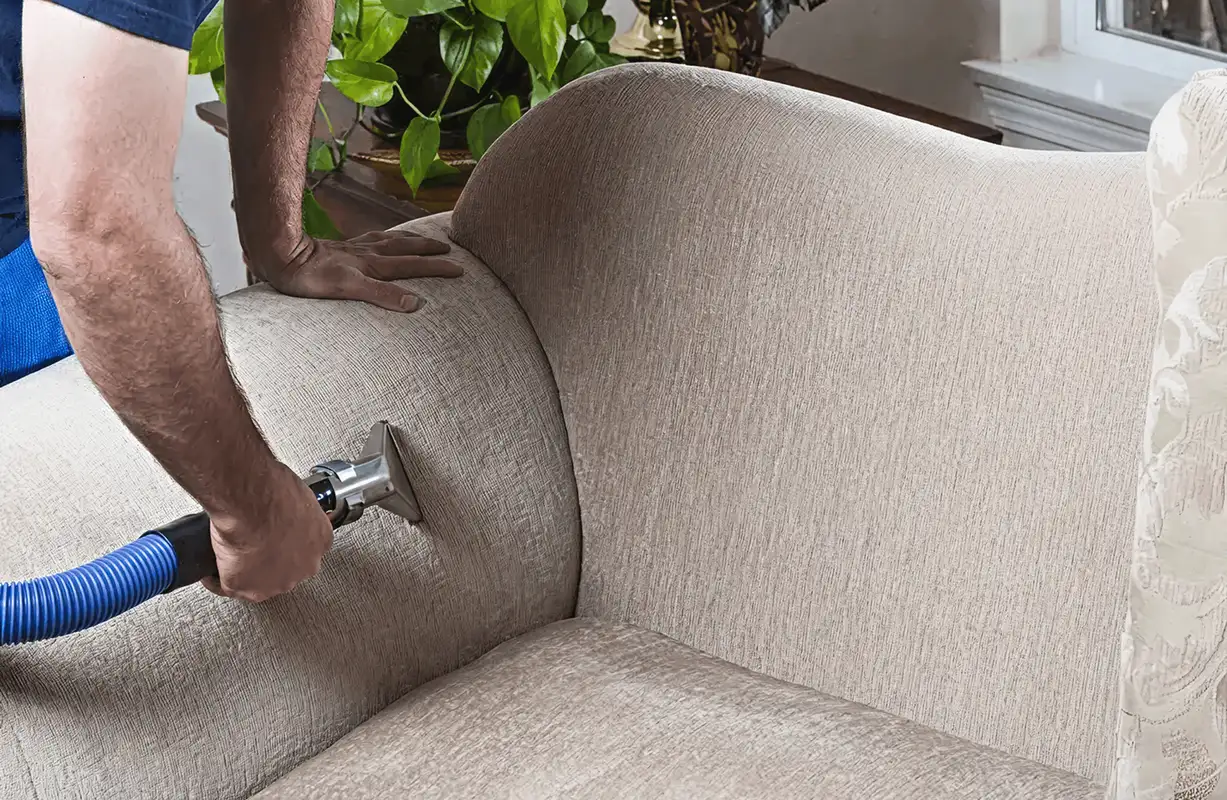 Professional upholstery cleaner deep-cleaning a fabric sofa with a handheld extraction tool and hose, Philadelphia, PA.